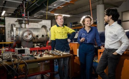 three people stand next to a table of wires and electronic equipment